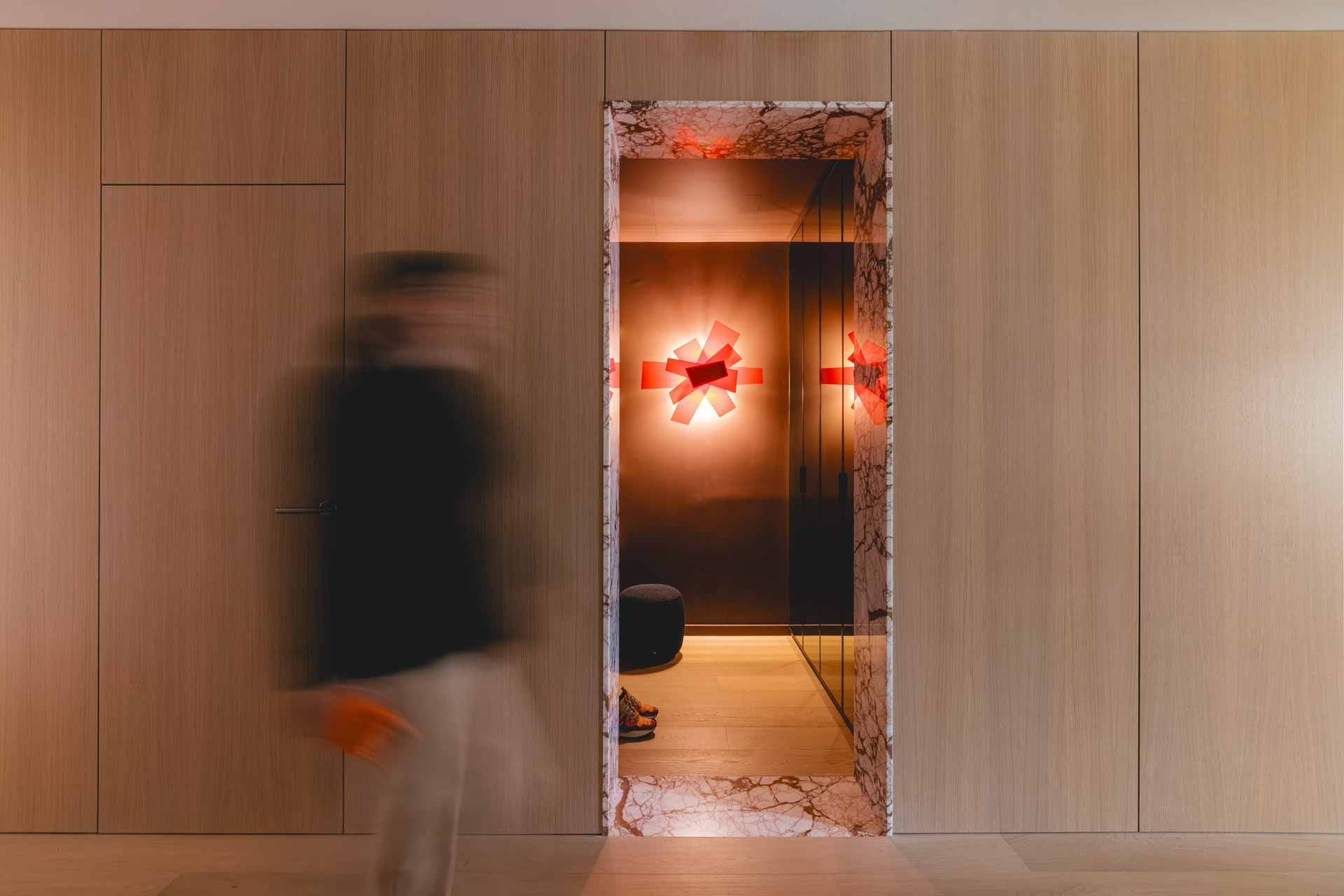 A figure in motion passing a marble doorway with a glowing red sculptural light.